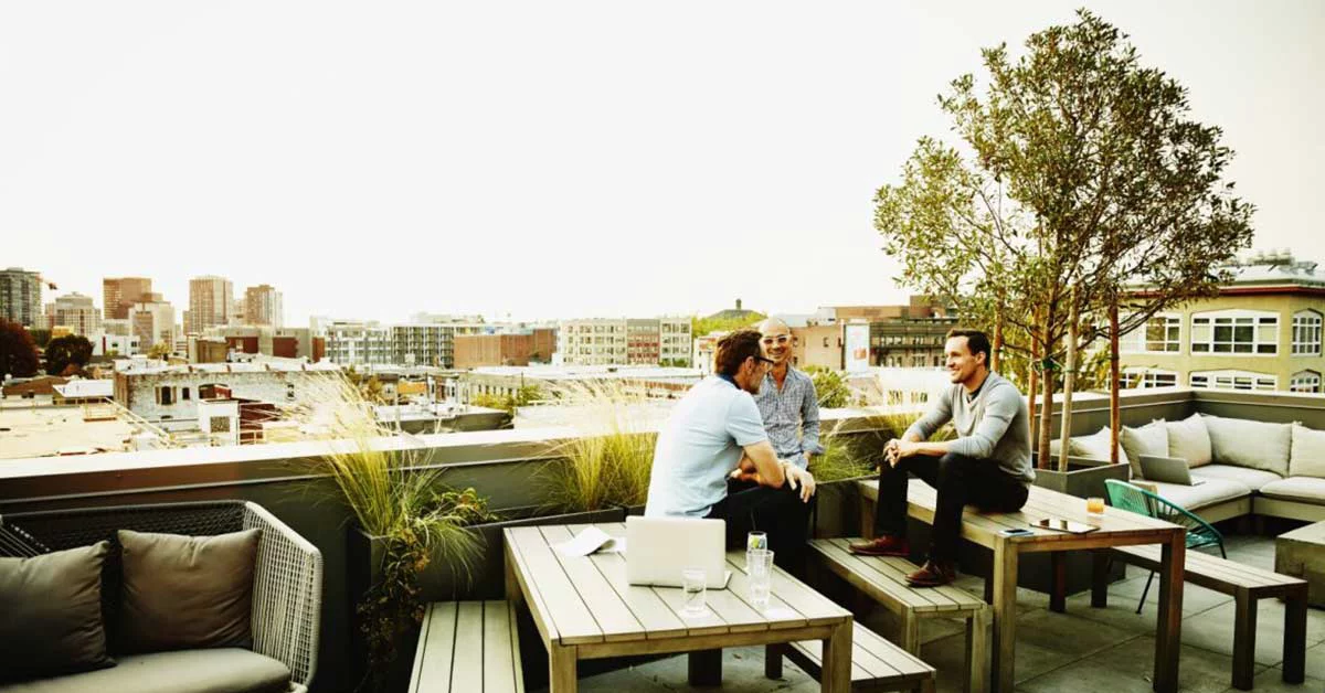 Three colleagues having informal meeting on terrace of office building on summer evening