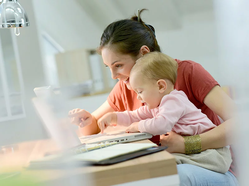 A mother typing at her desk with her baby.