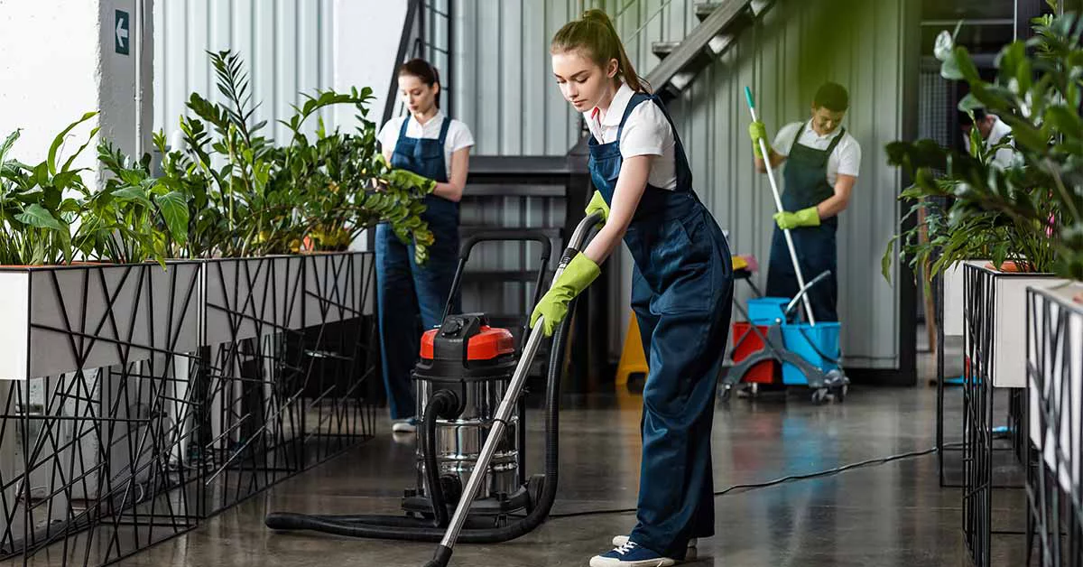 Two women are cleaning a room filled with various indoor plants