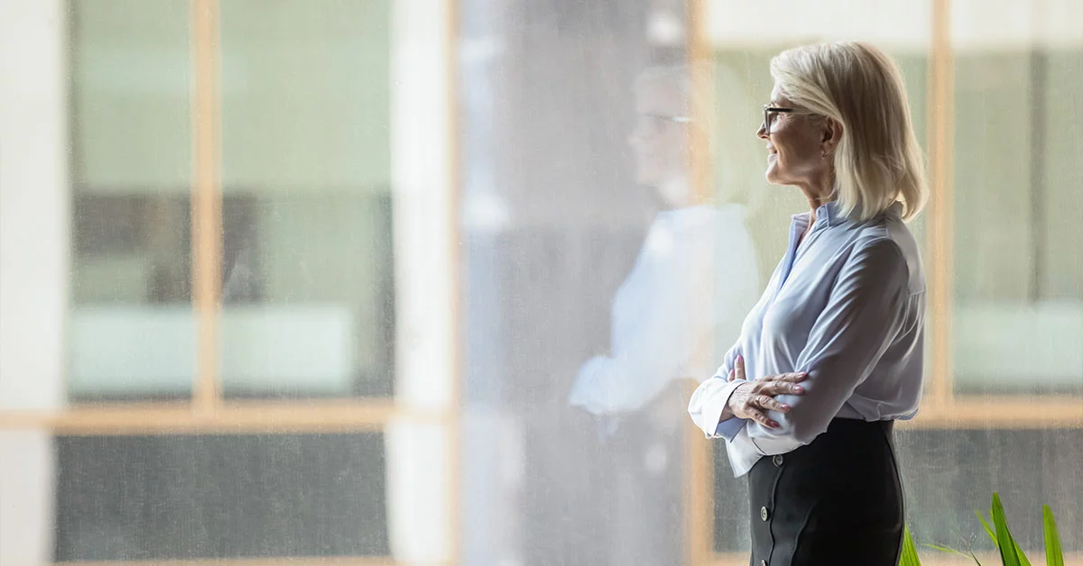 A business-suited woman stands by a window