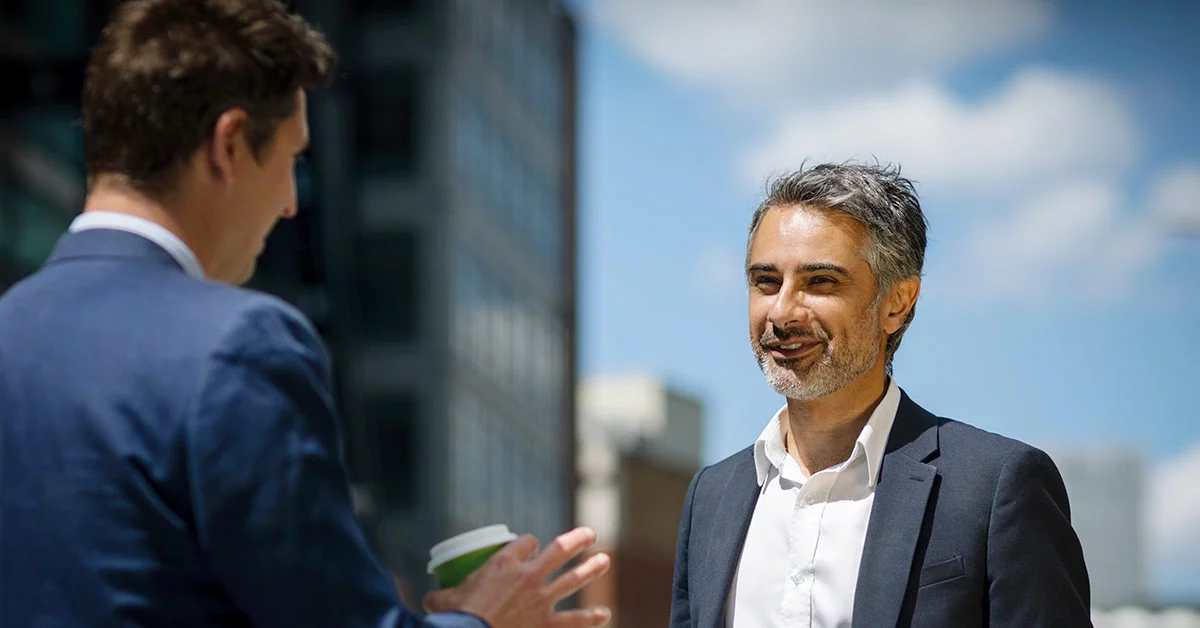 Two men in suits engaged in conversation outside a modern building.