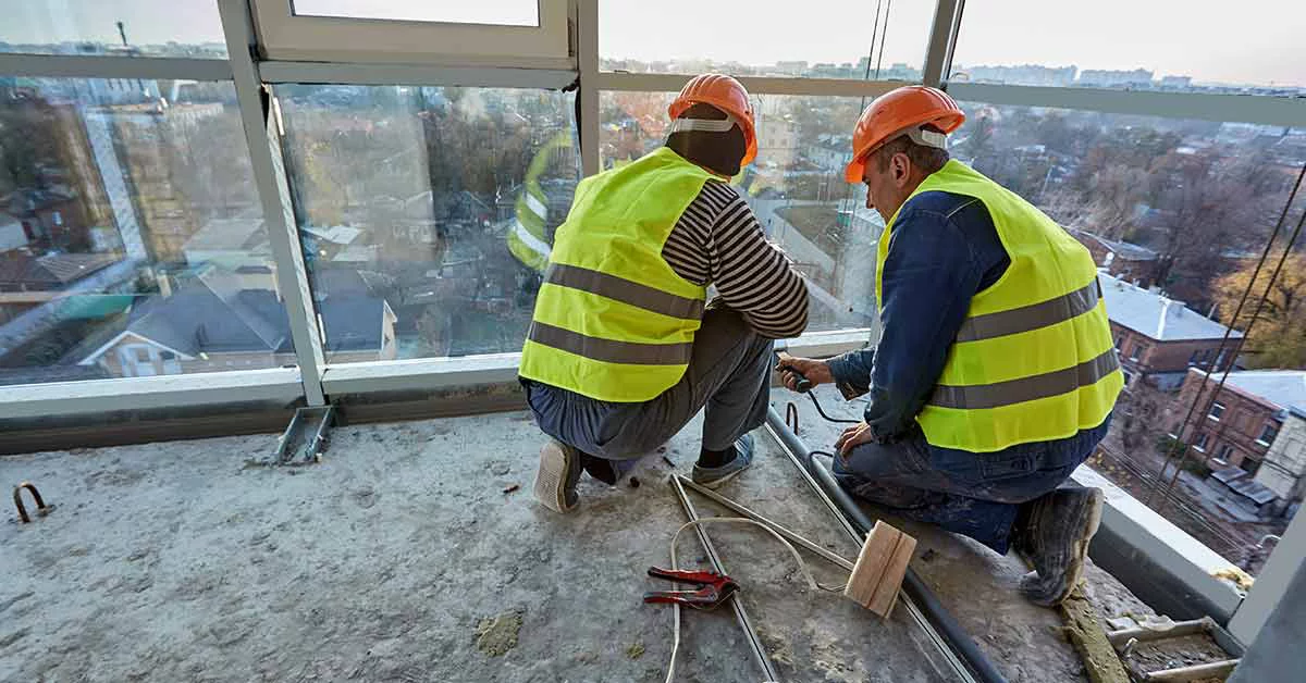 Two workers in protective clothing and safety helmets are installing plastic pipes in new flat.