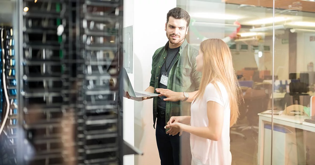 Two people standing in server room with laptop and discussing