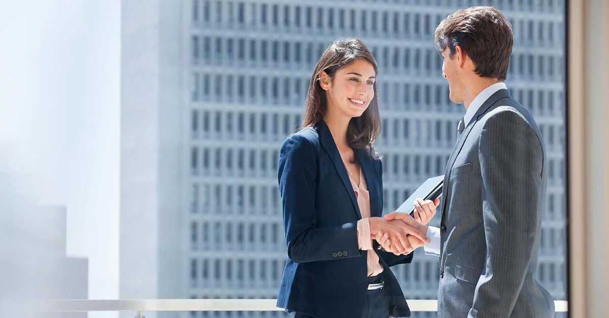 A man and woman engaged in a handshake outside a building