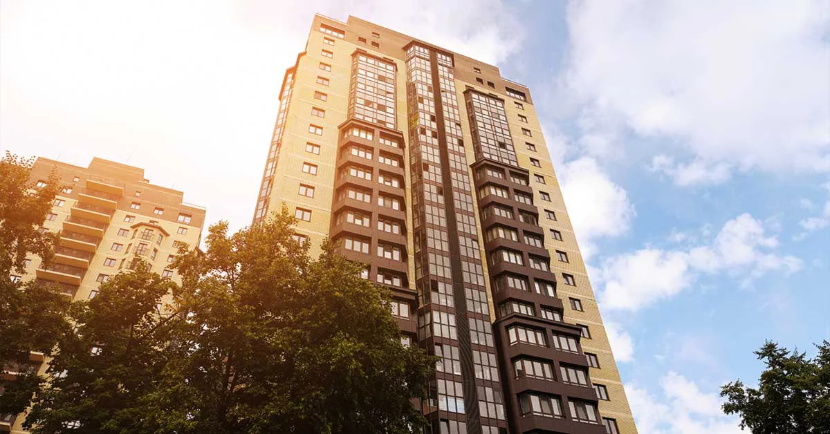 A tall building with numerous windows surrounded by lush green trees