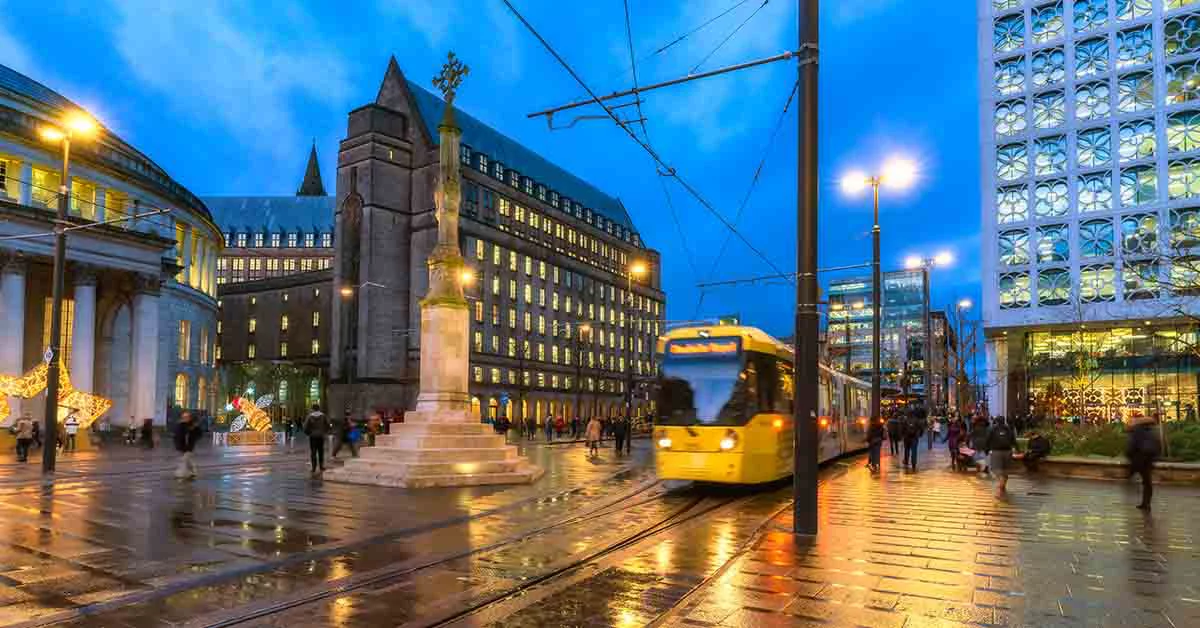 Manchester city centre, City tram approaching with pedestrians walking on the road.