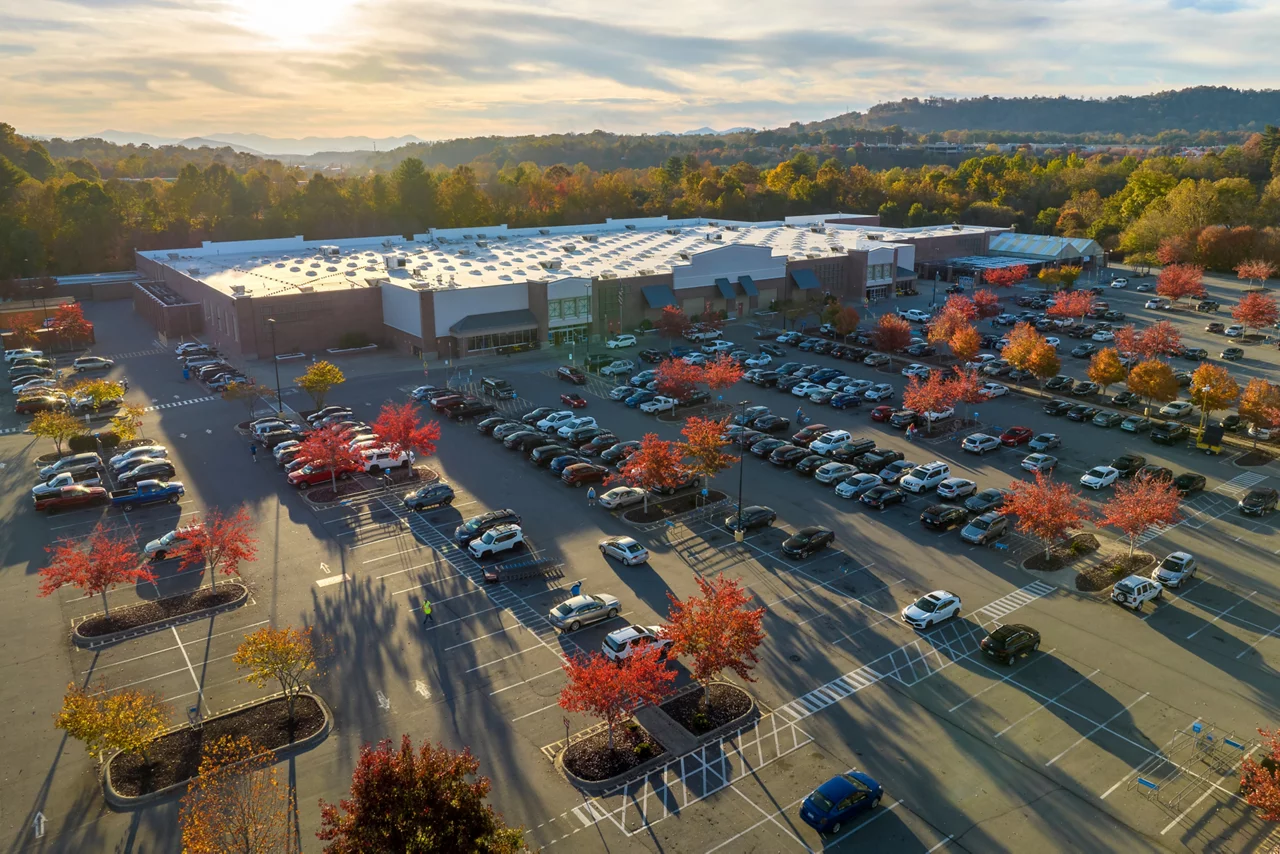 View from above of american grocery store with many parked cars on parking lot with lines and markings for parking places and directions. Place for vehicles in front of a strip mall center.
