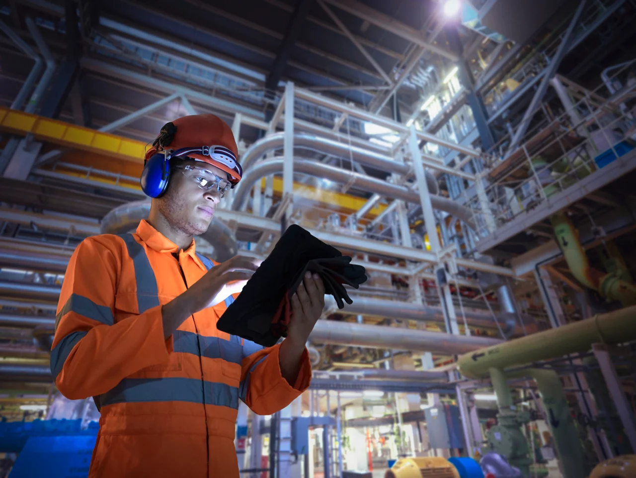 Worker in safety gear uses a tablet for digital compliance checks in an industrial facility.