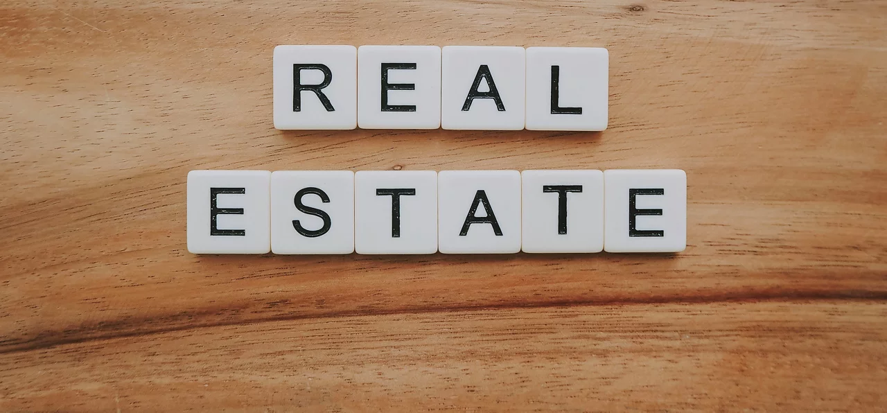 White letter tiles on a wooden surface spell out REAL ESTATE