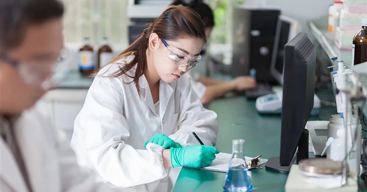 A woman in a lab coat focused on her work while using a computer in a laboratory setting