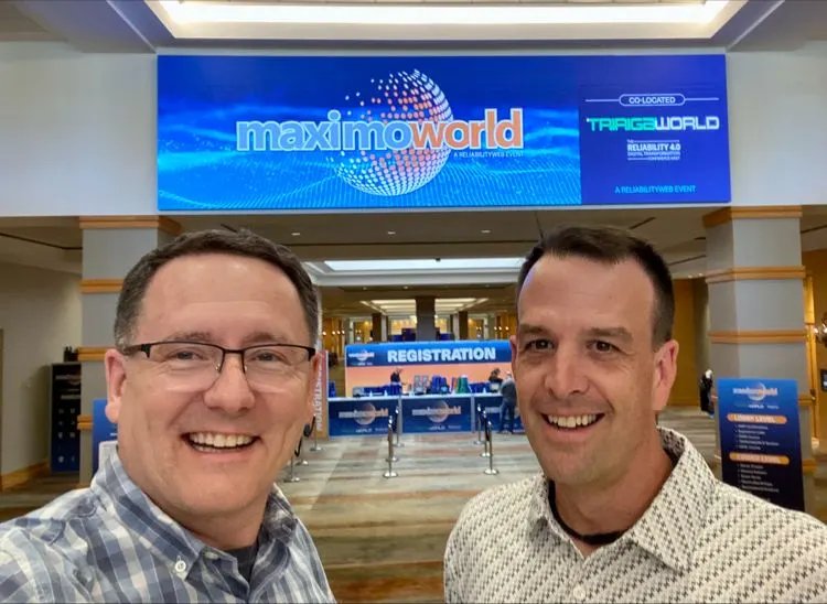 two professional men taking a selfie at what appears to be a conference or trade show venue. 