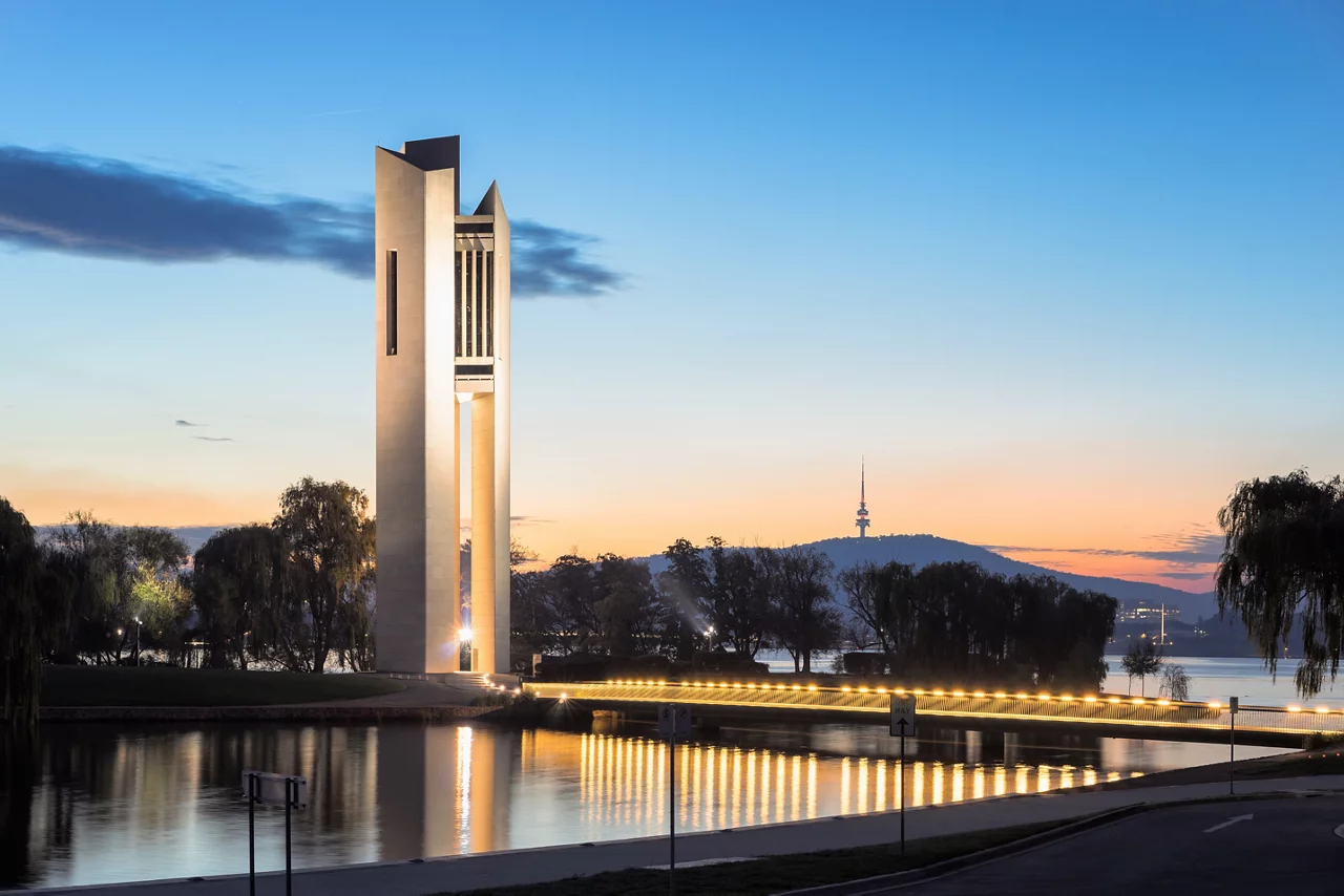 An elegant, modern bell tower, the National Carillon, illuminated at dusk on an island