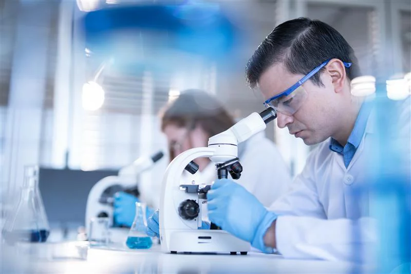 Male scientist in safety glasses using microscope in modern laboratory