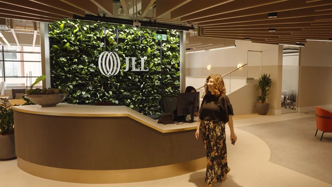 現代辦公室大廳，配有弧形接待台，有展示 JLL 標誌的植物牆，以及一名正在走過的女士。