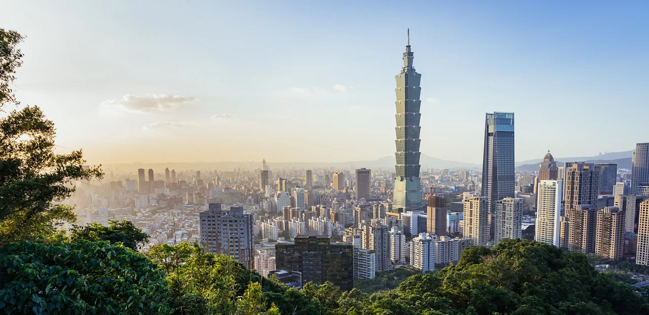 台北101大樓在黃金時刻主宰著城市天際線，從高處遠望，前景是蔥鬱的綠意。