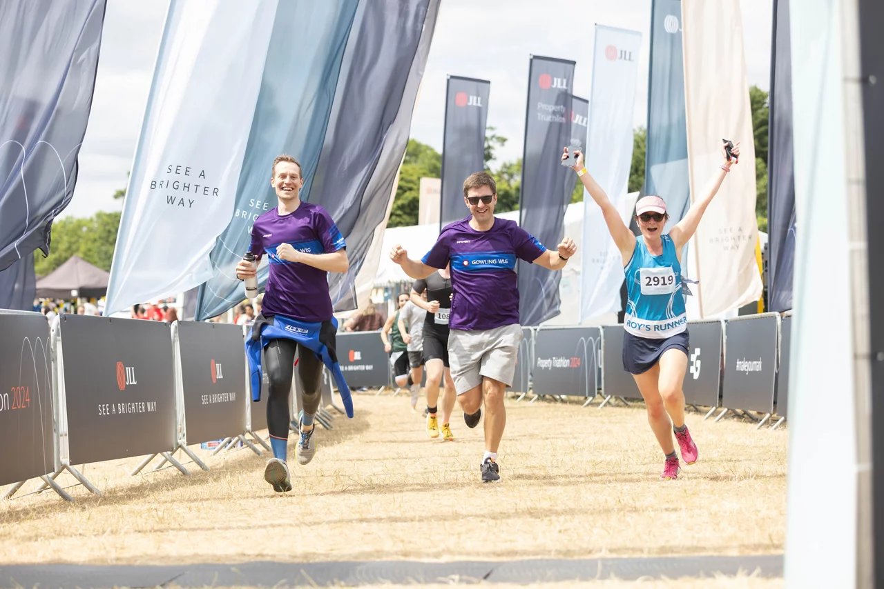 Runners crossing finish line at JLL-sponsored race event, surrounded by company banners and flags.
