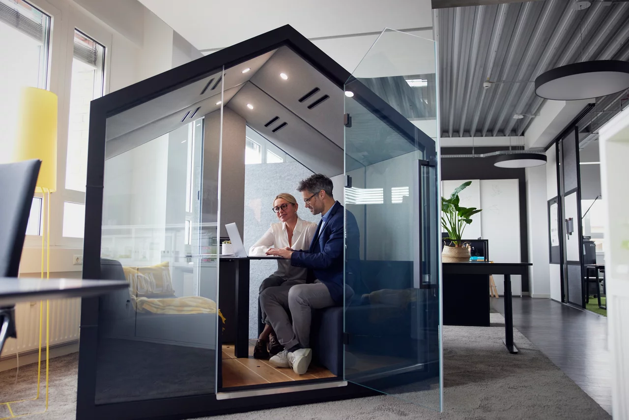 Business colleagues working on laptop sitting in office cubicle
