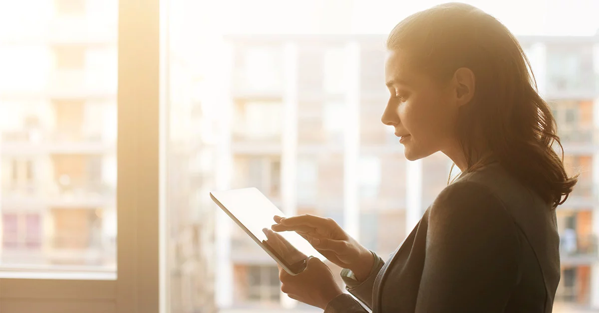 A professional woman dressed in a business suit is focused on her tablet.