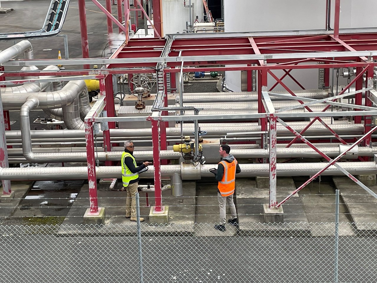Two construction workers in high-visibility safety vests stand on an industrial platform