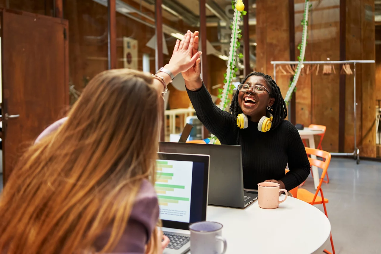 Professionals collaborate on laptops and share a celebratory high five