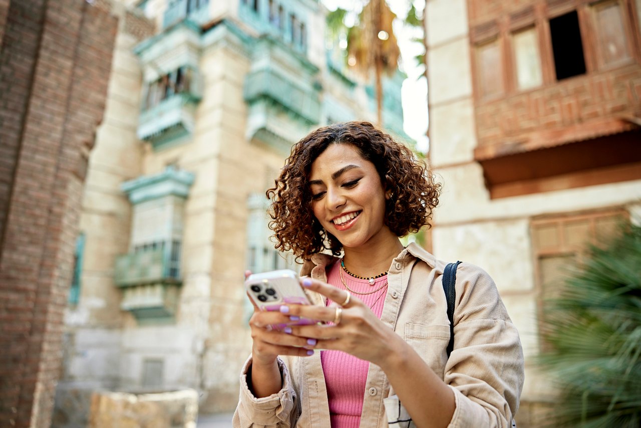 Waist-up view of casually dressed woman with curly brown hair looking at smart phone