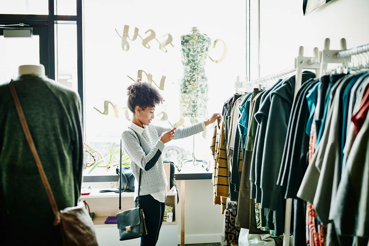 Woman taking photo of clothing with smartphone while shopping in boutique shop