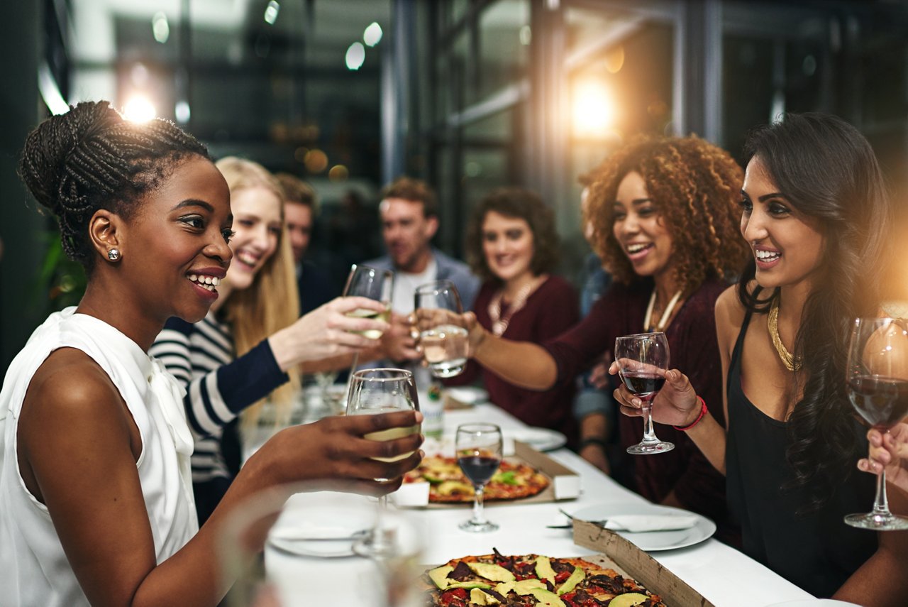 Group of friends toasting with wine glasses at restaurant table with pizza and appetizers