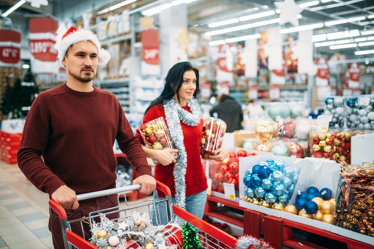 Couple holiday shopping with cart full of Christmas decorations in retail store