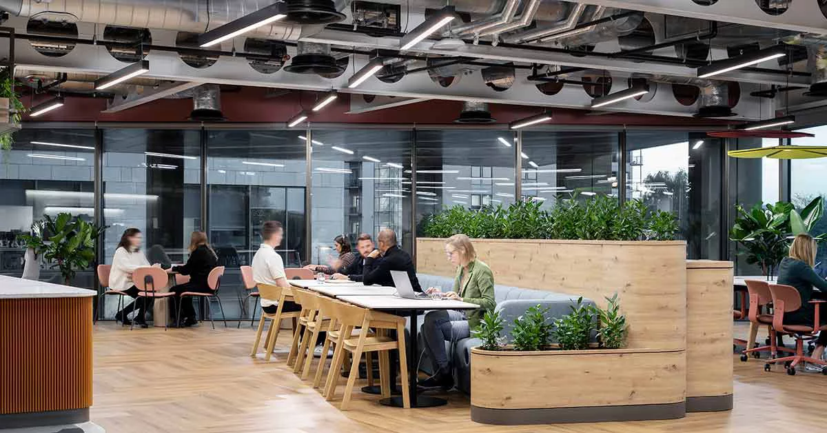 An office scene with people working at tables, focused on their computers in a collaborative environment.