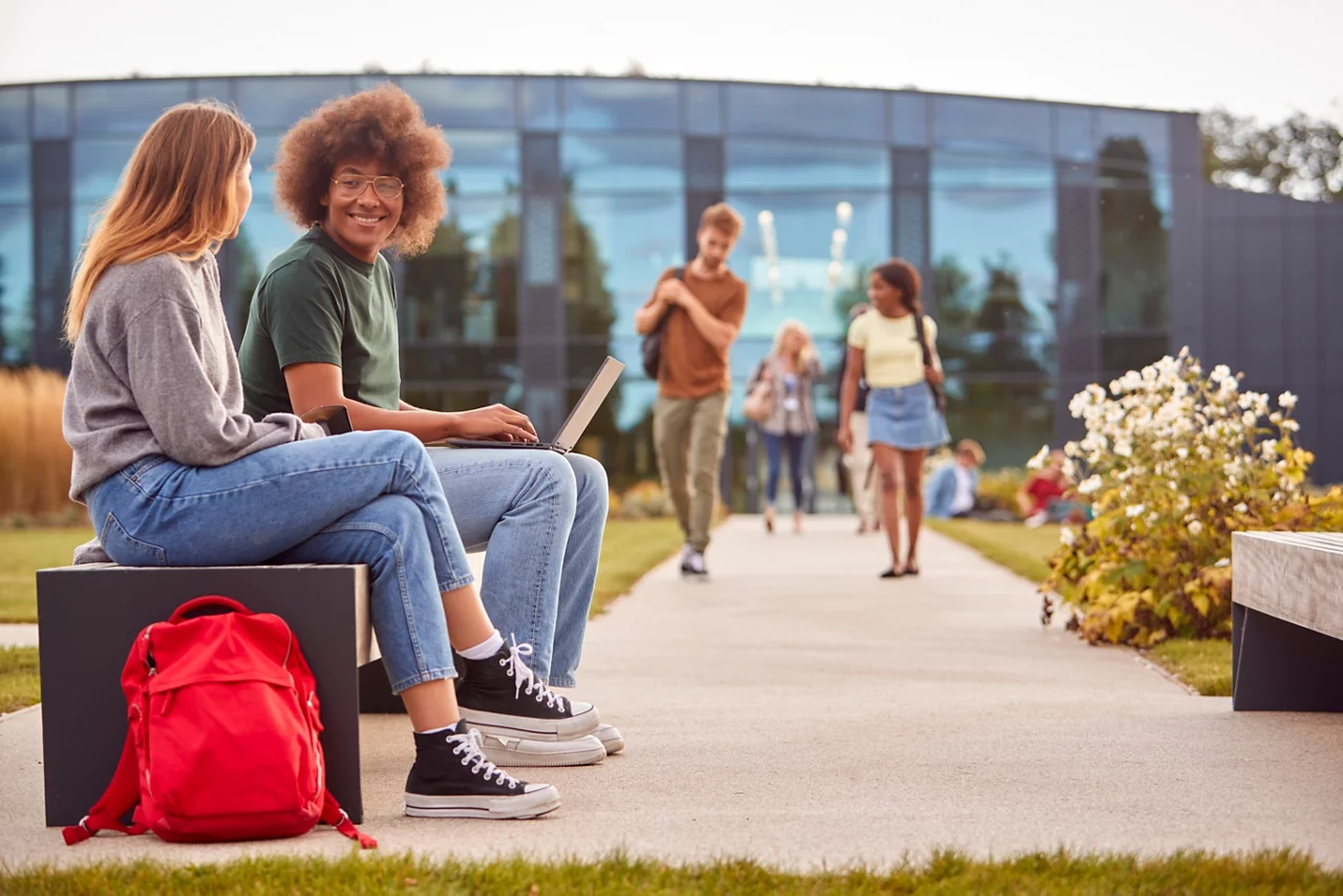 Male and Female college students sitting outdoors on campus working on laptop together