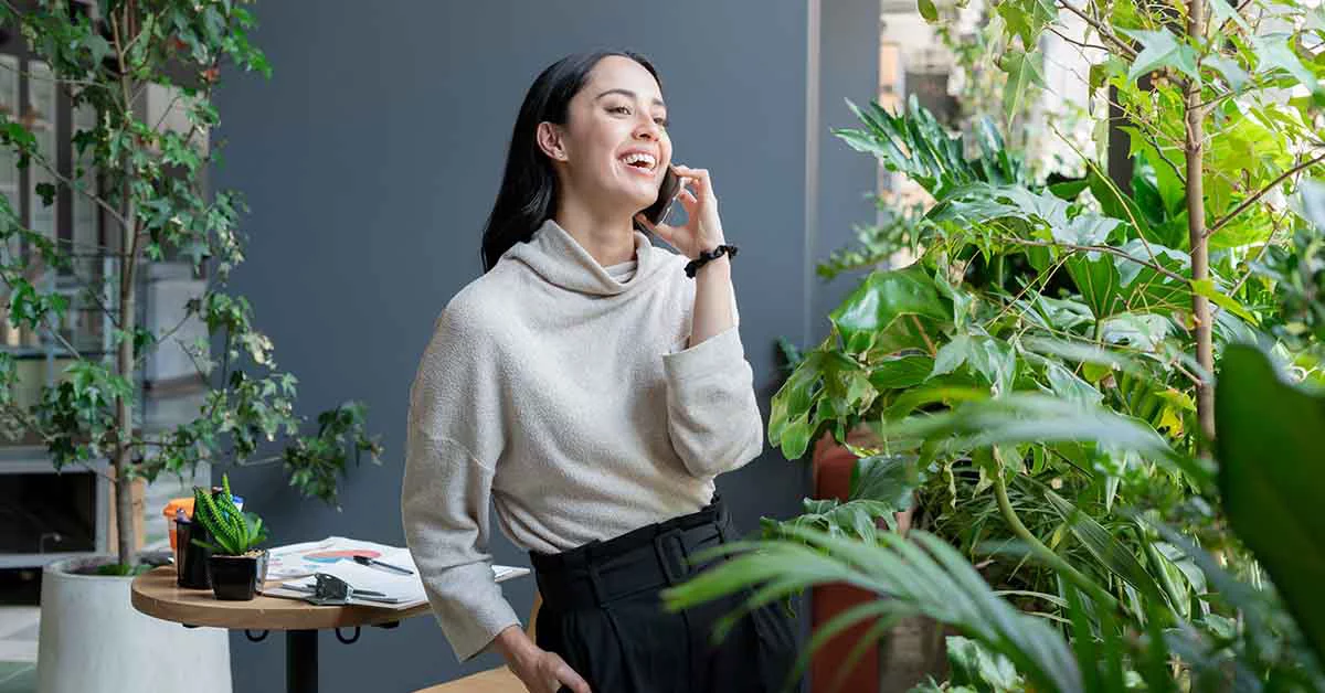 A woman standing near the garden area and smiling while talking on phone