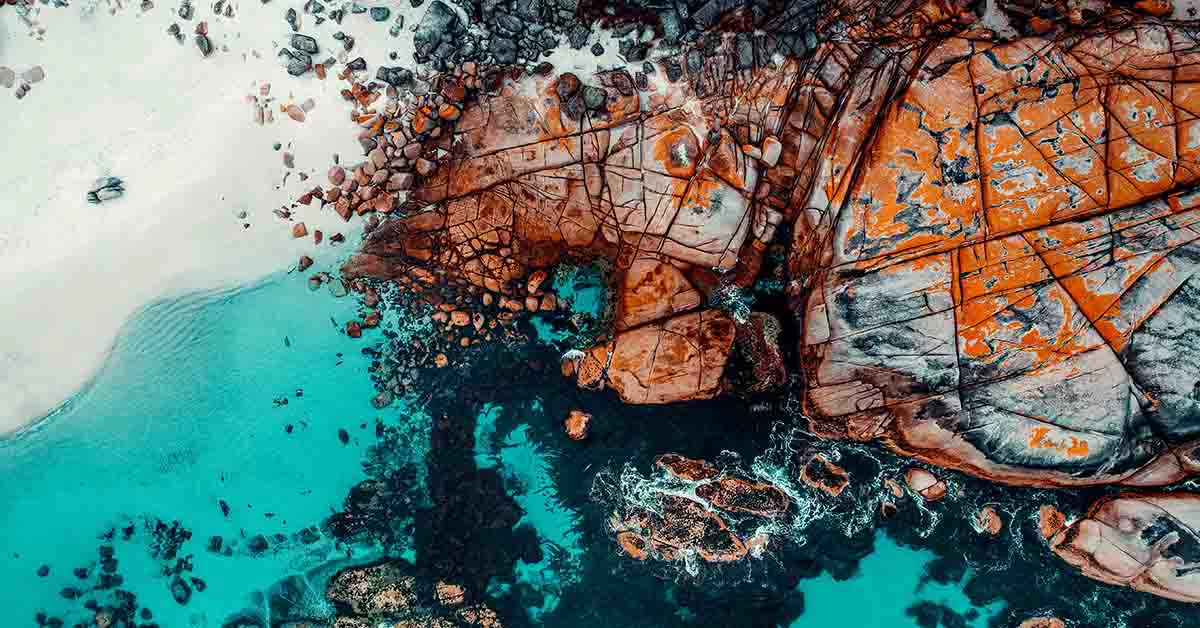 Aerial view showcasing the ocean's blue waves crashing against rugged rocks along the coastline.