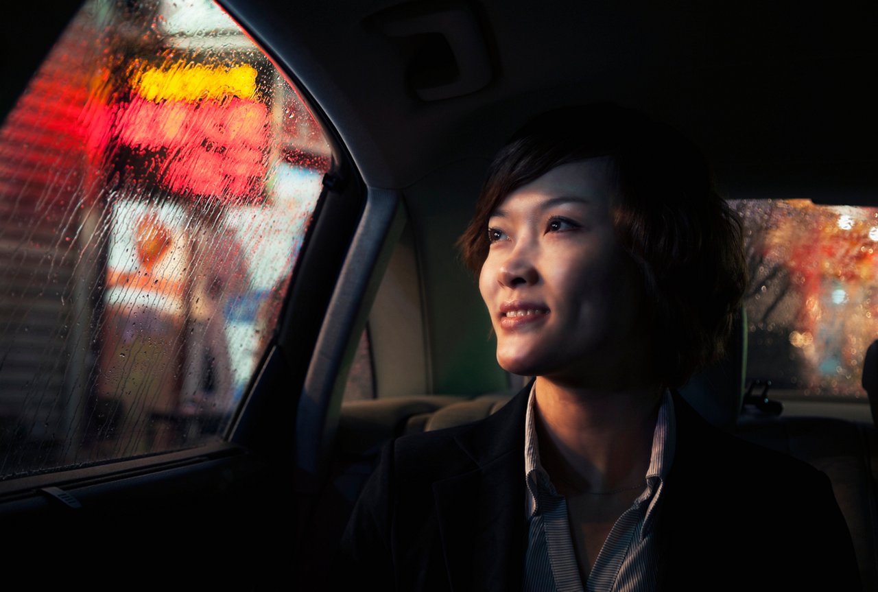 Contemplative Businesswoman looking out of car window through the rain at night in Beijing