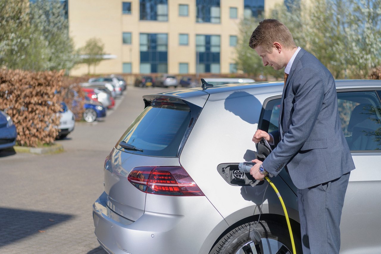 Businessman charging electric car at charging point in business park