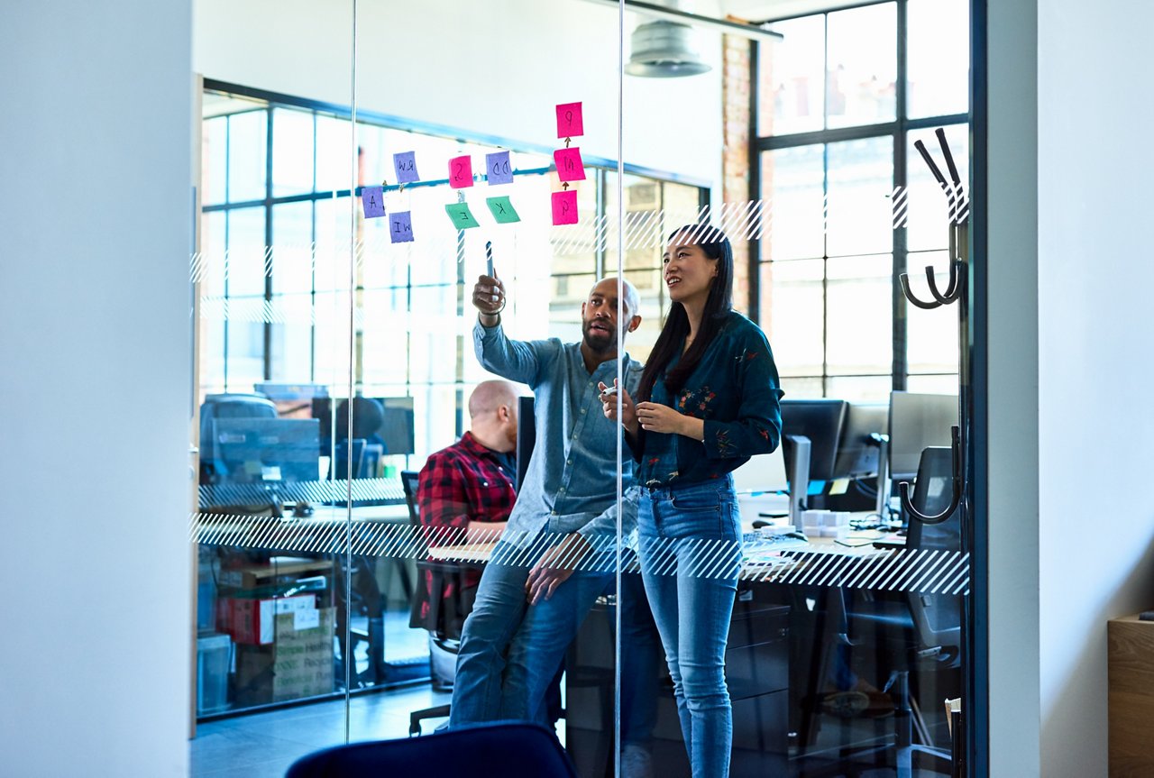 Businessman mentoring female colleague, discussing business strategy, using sticky notes to plan and solve problems, brainstorming, innovation