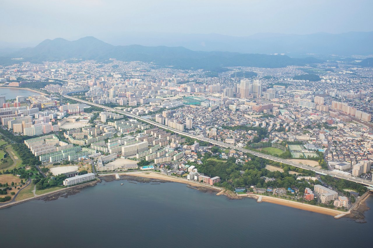 密集した都市開発、背景の山々、中心部を通る主要高速道路を備えた沿岸都市の航空写真。