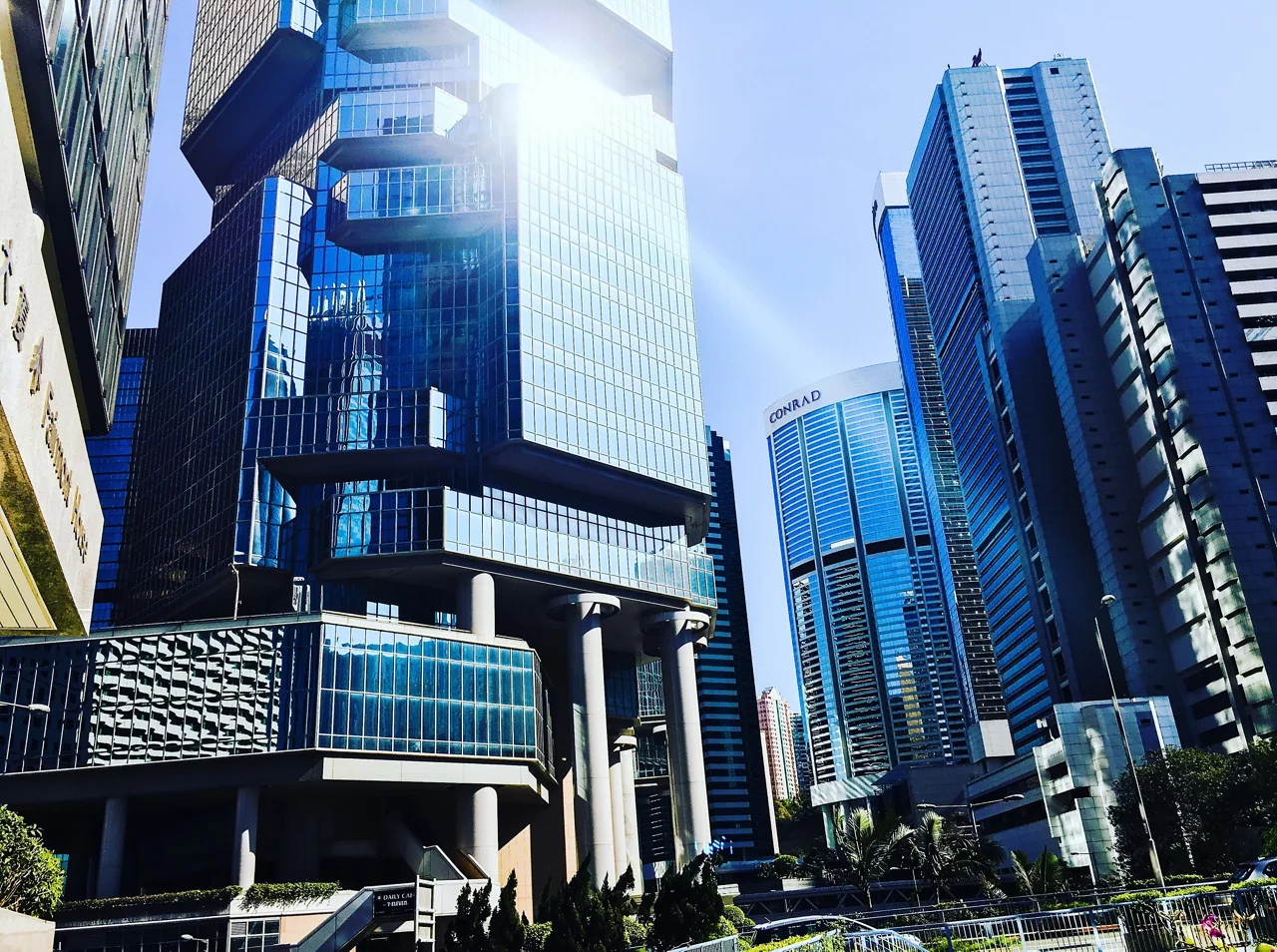 A low-angle shot captures a cluster of modern skyscrapers with predominantly blue glass facades, reflecting the bright sunlight.
