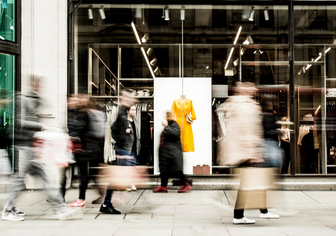 Motion blurred people walking past shop window 