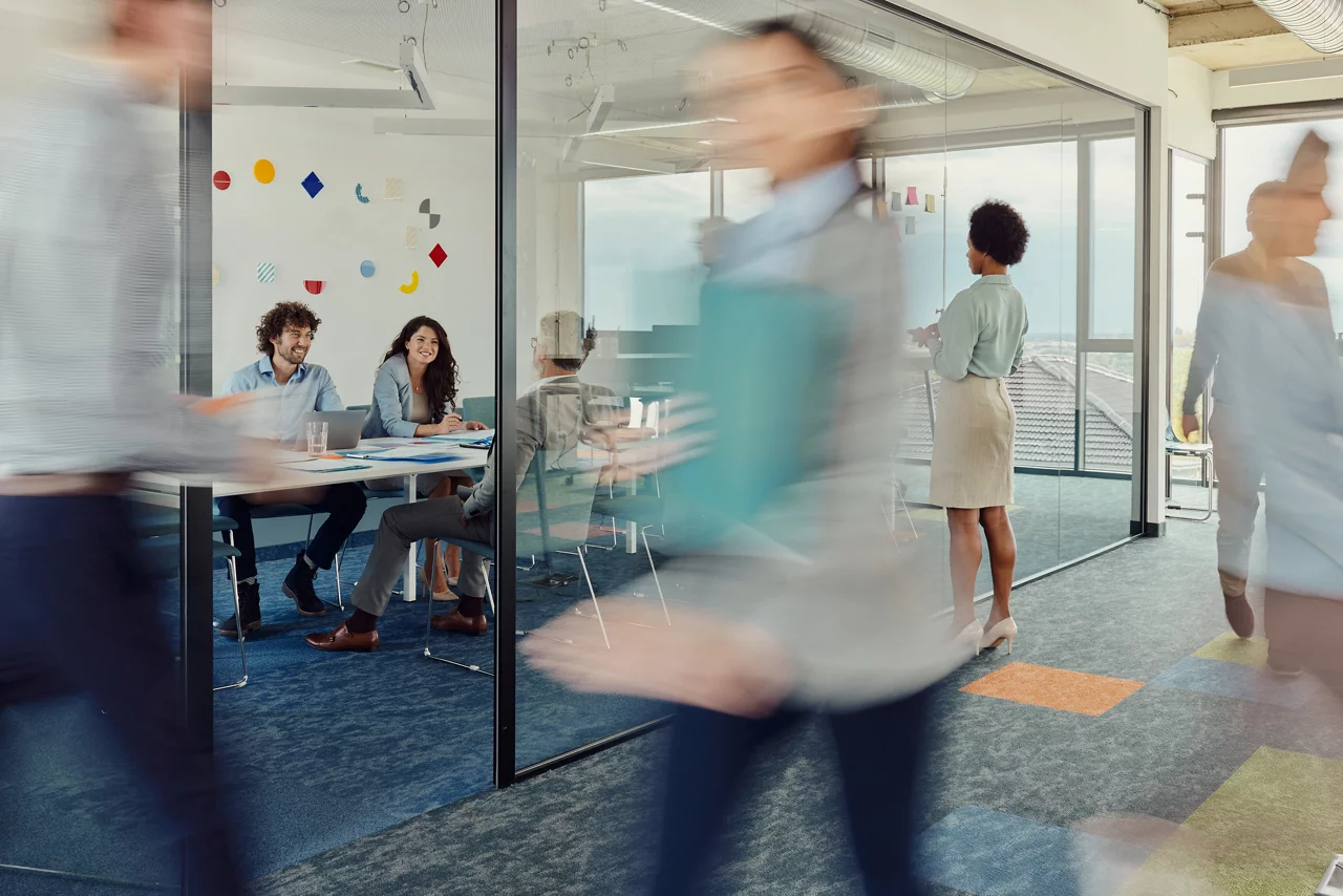 Large group of business people working in a modern office. Focus is on happy colleagues inside of glass office and black businesswoman.