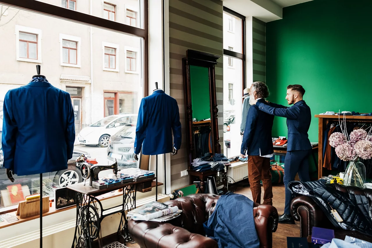 A retail assistant helping a mature customer with a suit jacket he is trying on in a menswear store.