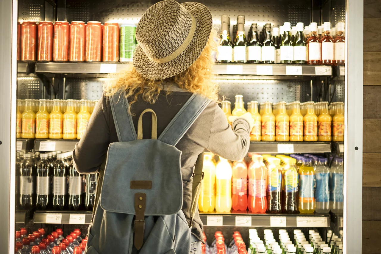Travel woman viewed from back choosinf beverage in a fresh fridge
