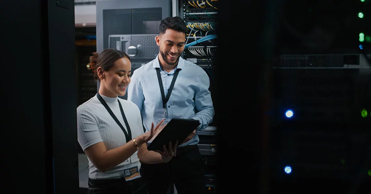 Two employees smiling while looking at the tablet inside data centre