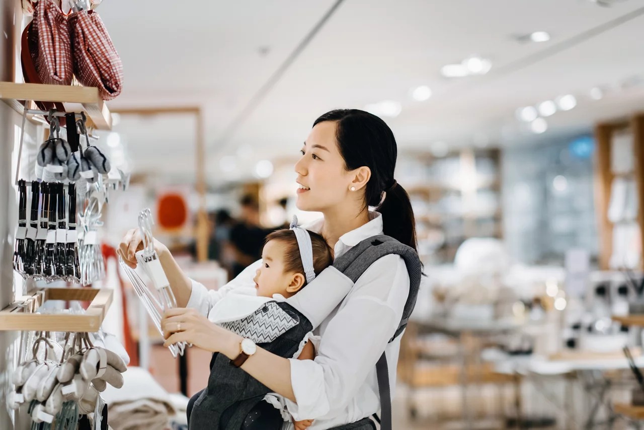 Beautiful young Asian mother carrying baby girl shopping for home essentials in shop