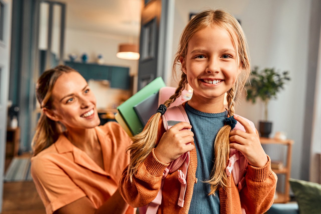 Preparing for school.Buying fresh school supplies,packinga backpack full of notebooks.Portrait of a girl with pigtails going to school, her mother puts colorful textbooks in her backpack from behind.