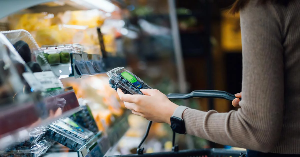 A woman checking her mobile phone while reviewing her grocery items at the checkout counter.