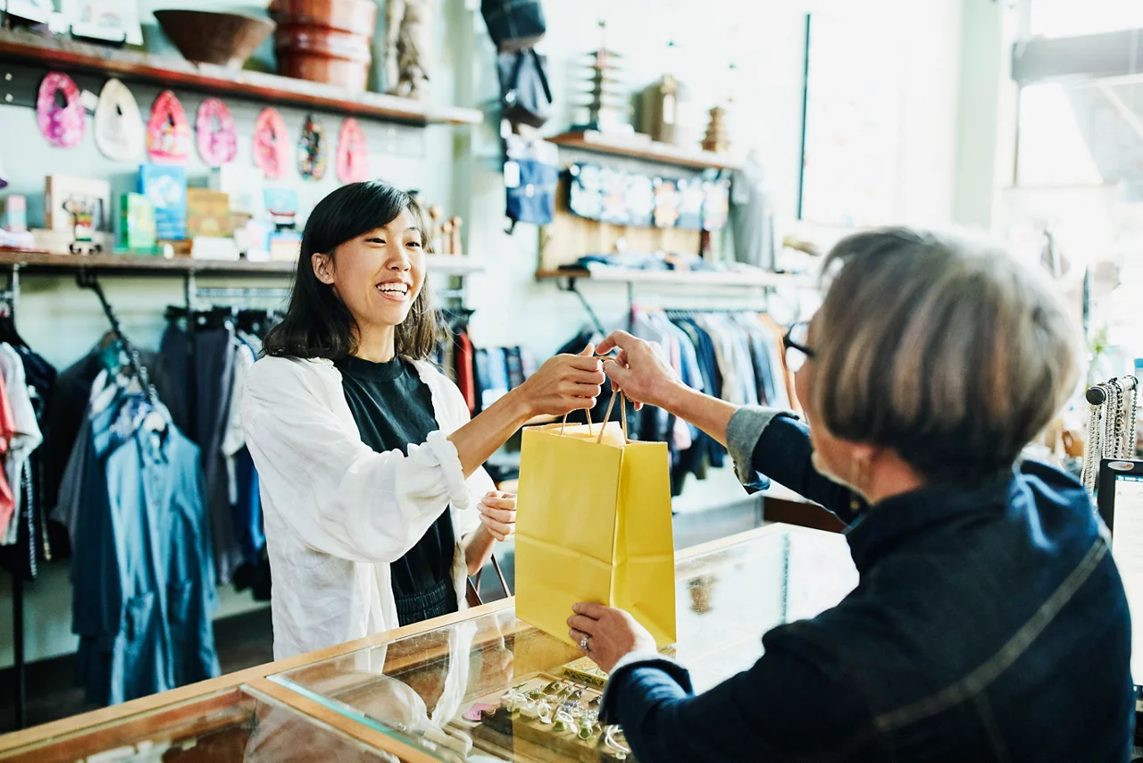 Shop owner handing bag to client after shopping in clothing boutique