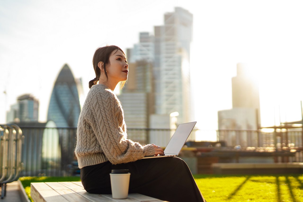 Young Asian businesswoman working on laptop outdoors, sitting on the bench in rooftop garden