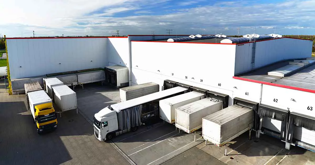 A spacious warehouse building with multiple trucks parked outside, indicating active shipping and receiving operations.