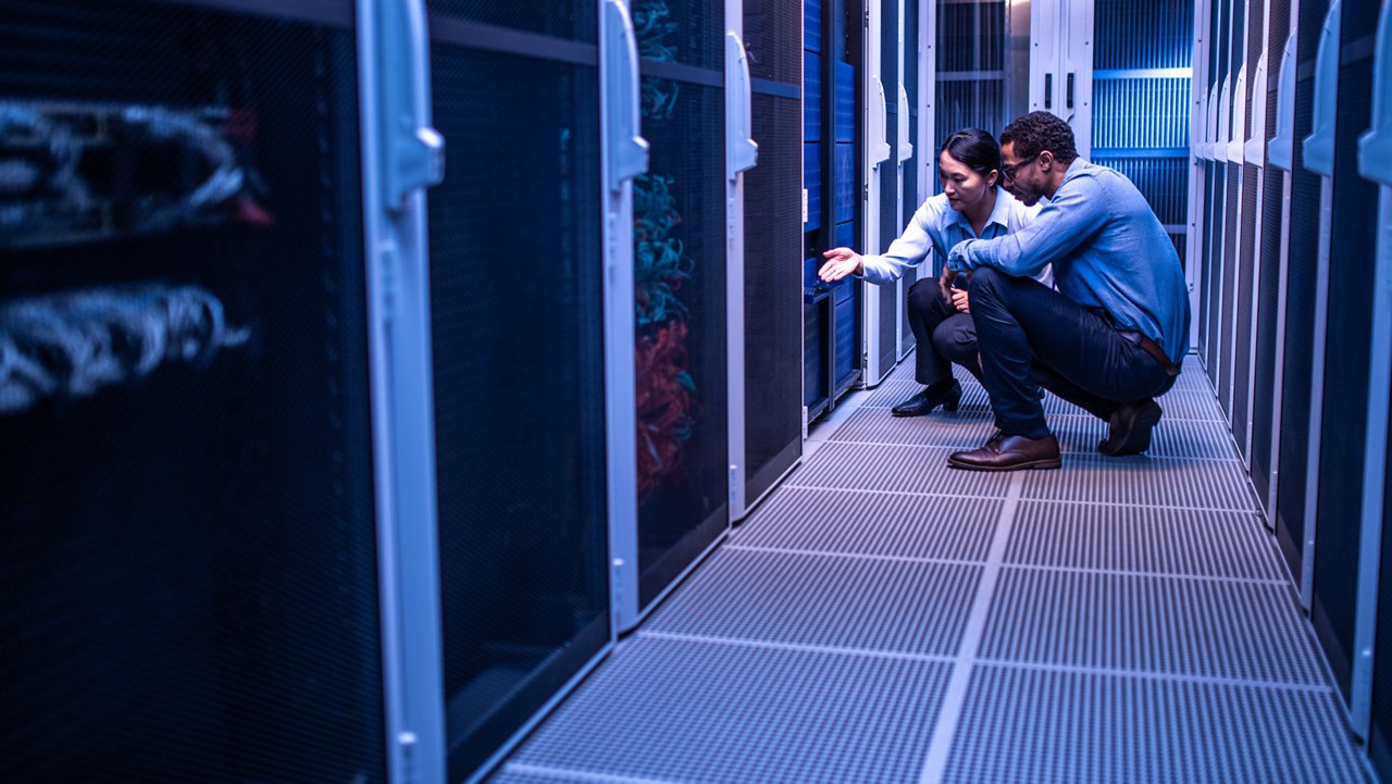 Male and female IT engineers checking servers in server room.