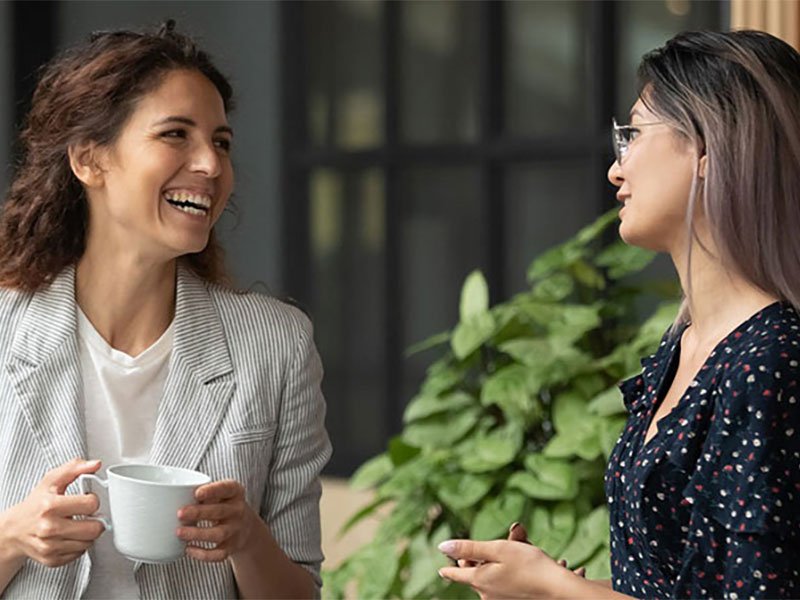 Happy female colleagues talking laughing during break in work space